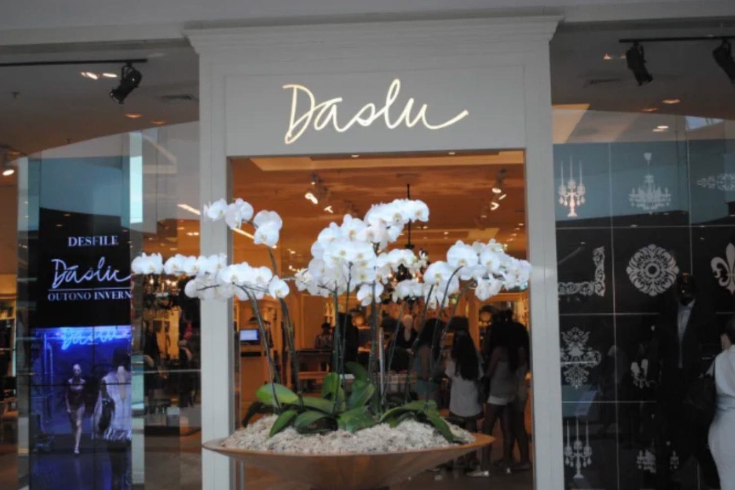 Entrada da Daslu, com orquídeas brancas e a TV da loja anunciando o desfile